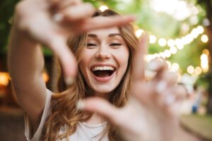 happy young girl showing frame with fingers while standing at the park